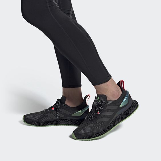 a person is wearing a pair of black adidas running shoes with green and red accents. they are standing on a white surface. the shoes have a black knit upper, black laces, and a black boost midsole. the outsole is black with green accents. the adidas logo is visible on the tongue and heel of the shoe.