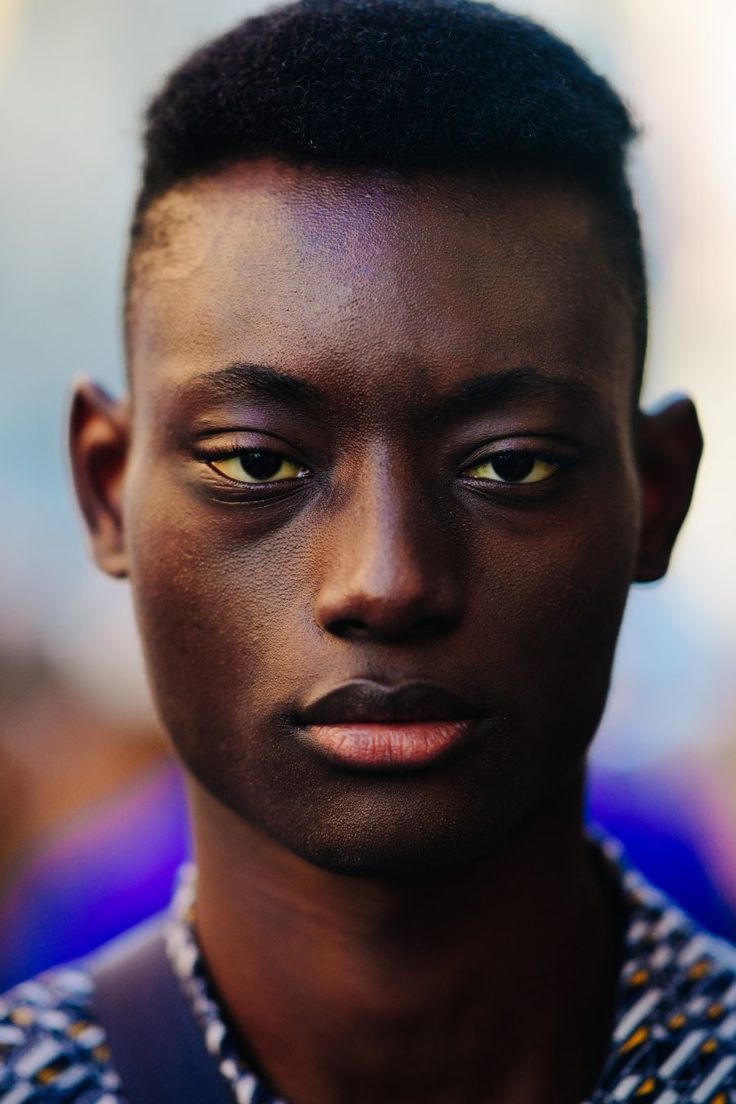 a closeup portrait of a young man with dark skin. he has short, cropped hair and a serious expression on his face. the photo focuses on his facial features, highlighting his eyes, nose, and lips. he is wearing a shirt. the background is blurred.