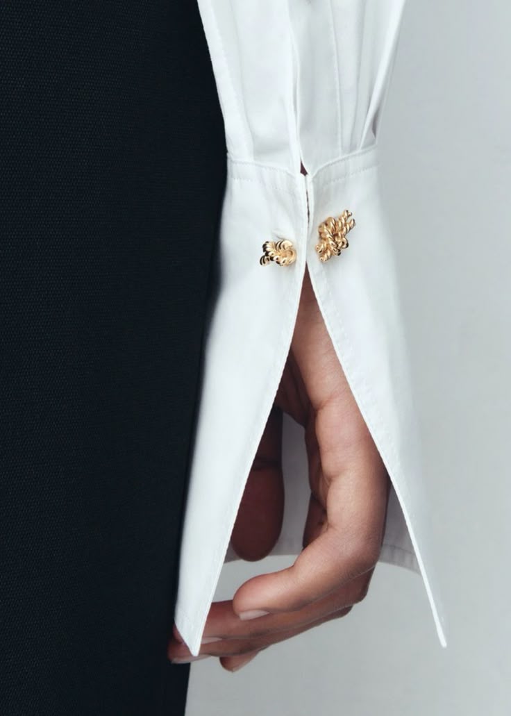 closeup shot of a person's hand with a white shirt cuff fastened with gold cufflinks. the person is also wearing a darkcolored dress. the focus is on the sleeve, cufflink, and hand.