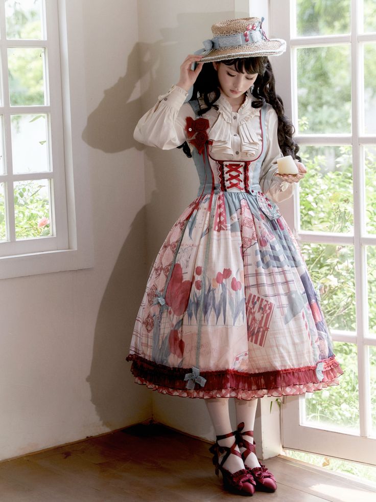 a woman wearing a colorful and stylish lolita fashion dress and a widebrimmed straw hat is posing by a window. the dress features a mix of patterns and colors, including floral, plaid, and stripes, in shades of red, blue, and white. she is also wearing a white blouse with lace details. the photo is taken indoors in a room with white walls and large windows, allowing natural light to brighten the scene.