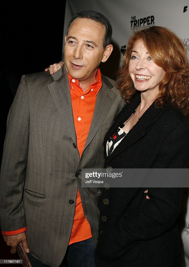 a man in a grey suit and orange shirt smiles and poses with his arm around a woman in a black jacket. they are at a photocall for the premiere of a movie called "the tripper".