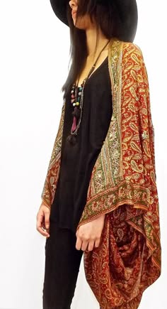 a woman wearing a vintagestyle paisley patterned shawl over a black top and hat. she is smiling and posing for the camera. her look is boho chic and trendy.
