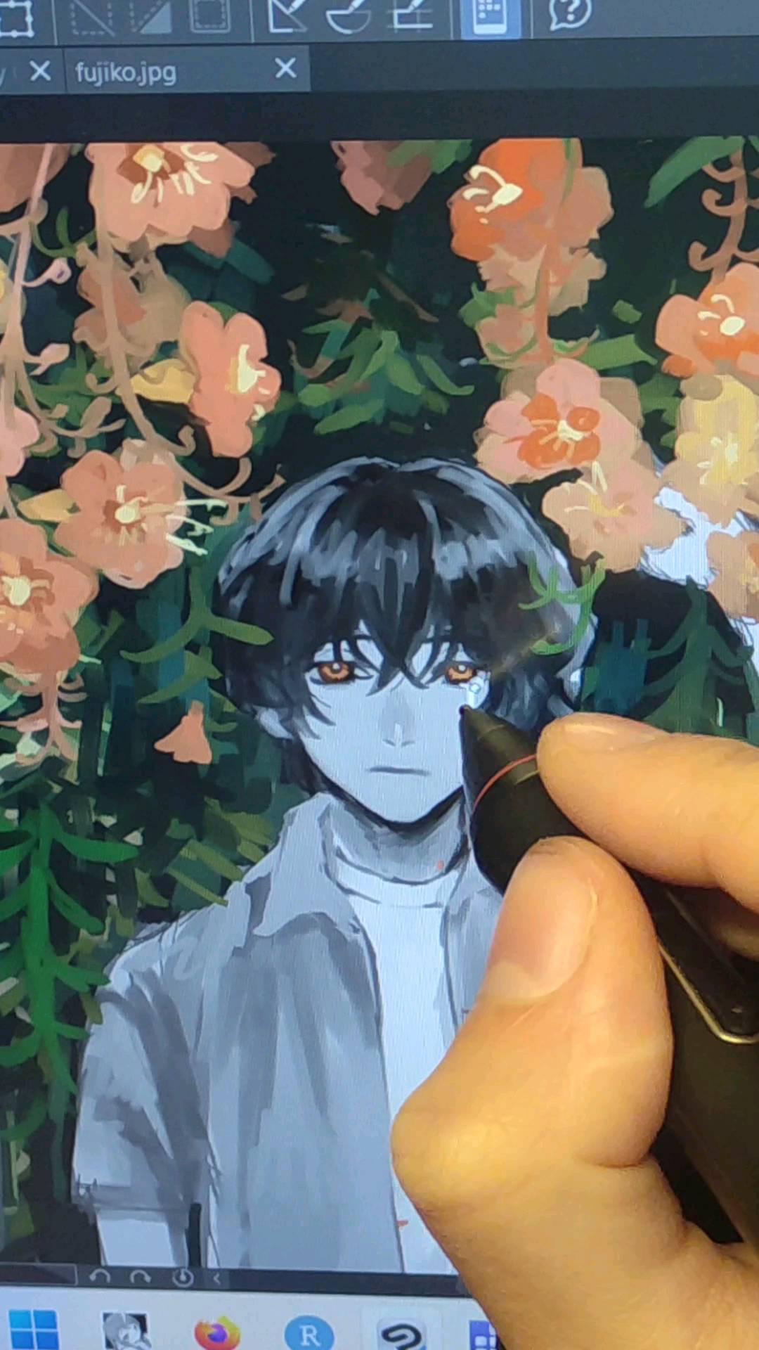 the image shows a closeup of a person's hand using a stylus to digitally paint on a graphic tablet. the artwork on the screen depicts a stylized anime or mangastyle portrait of a young boy with dark hair, who appears to be slightly melancholic. he's positioned against a backdrop of lush, peachtoned flowers. the artist's hand is prominently featured, holding the stylus and emphasizing the creative process of digital painting. the screen also displays the file name "fujiko.jpg" and the interface of the digital painting software. the overall aesthetic is artistic and slightly melancholic.