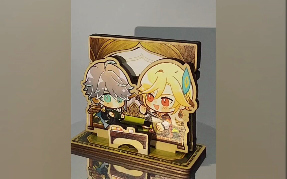 a close up image of a chibi anime figurine cut out of wood,  showing two characters sitting at a table in a cozy setting. the characters are both male and are small with big eyes and cute expressions. they are  displayed on a wooden stand and look like they are about to have a conversation.