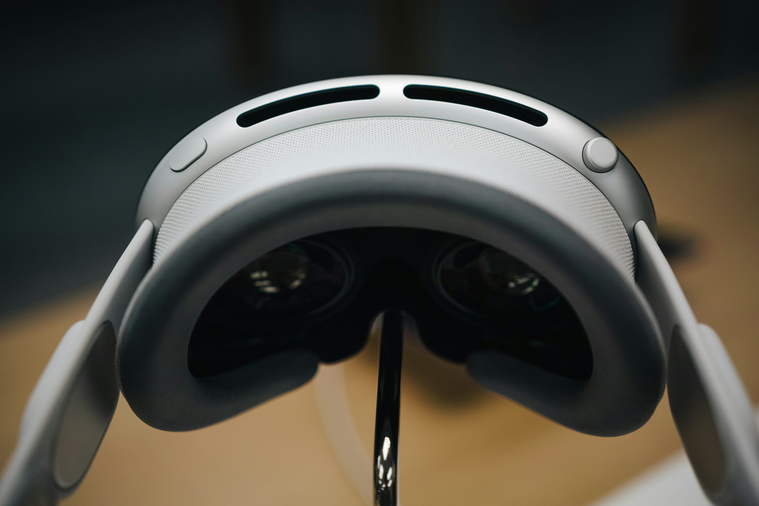 a closeup shot of an apple vision pro vr headset on a stand, viewed from the inside. the focus is on the interior components of the headset, including the lenses and padding, with the exterior details like the vents and dial visible on the top. the stand is a simple, thin, metallic support holding the headset in place.