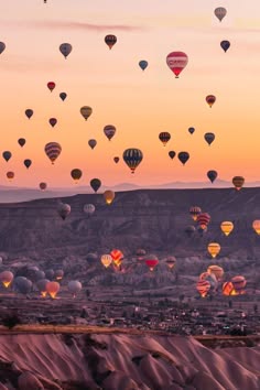 a beautiful view of hot air balloons floating in the sky over a rocky landscape.  the sky is a light blue with white clouds. the balloons are in different colors and sizes. some of the balloons are even reflecting the sunlight.  there are many people enjoying the view of the balloons. the image looks like it was taken in the early morning or late evening, as the sun is low in the sky and the light is soft. the image is peaceful and serene.  the photo is a great example of how beautiful and amazing the world can be.