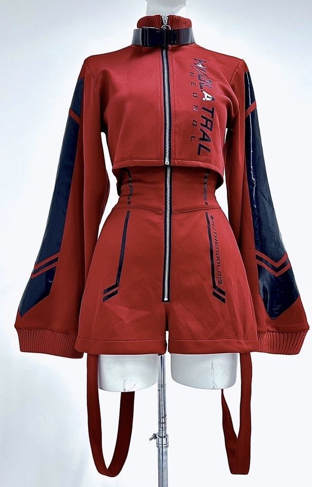a red twopiece outfit consisting of a cropped jacket and highwaisted shorts is displayed on a mannequin. the jacket has long sleeves with shiny dark blue accents and text on the chest. the shorts have a zipper down the front and matching dark blue accents. the outfit also features a black belt and long hanging straps.