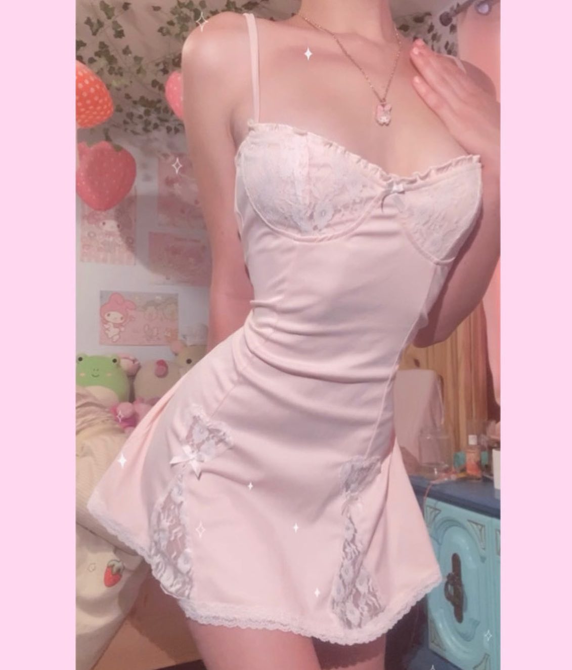 the image shows a young woman wearing a pale pink slip dress. the dress has lace trim at the neckline and hem and features a fitted bodice and a flared skirt.  she is standing in what appears to be a bedroom with a pastel aesthetic, including strawberry decor and soft lighting. the overall vibe is very feminine, romantic, and "kawaii" (cute). the woman's pose and expression are suggestive but not overtly sexual.