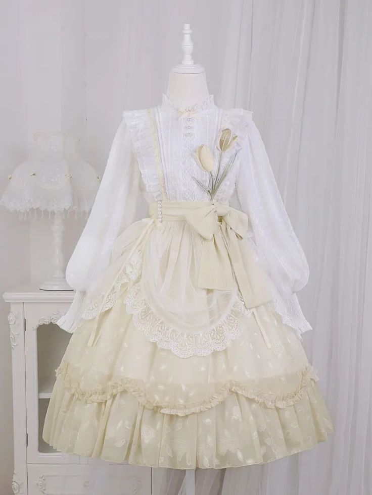 this image showcases a full, elaborate lolita fashion dress in shades of cream and white. the dress features a ruffled, highnecked blouse with delicate lace trim, paired with a voluminous skirt adorned with intricate lace detailing and floral patterns. a matching apron with a large bow at the waist adds to the sweetness of the design. the dress is displayed on a mannequin positioned against a white backdrop, emphasizing its intricate details and the overall romantic and feminine aesthetic.
