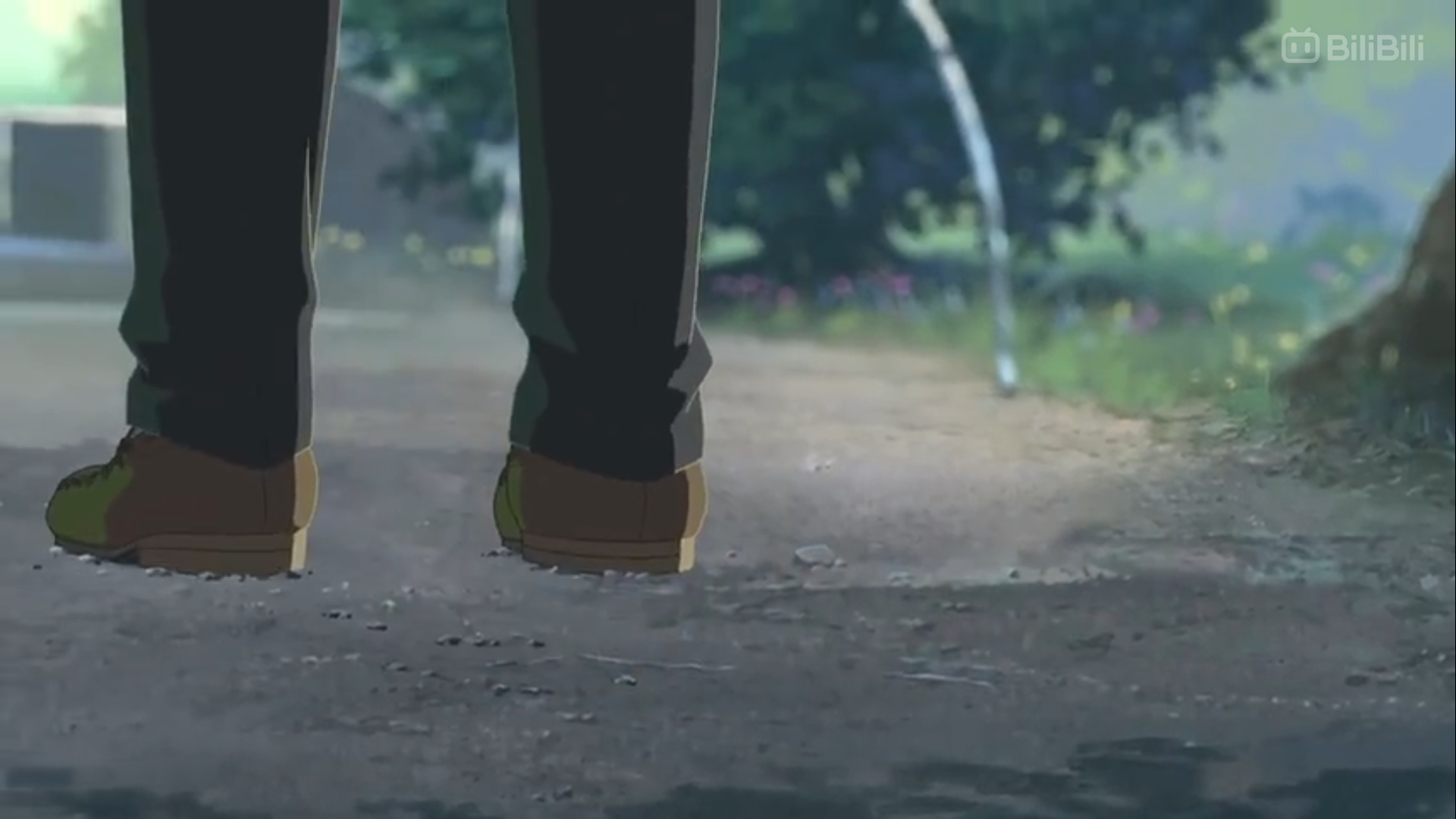 the image shows the back of a person's legs and feet as they stand on a dirt path. they are wearing brown shoes and dark pants. the path is surrounded by grass and trees, suggesting a natural, outdoor environment.  the lighting is soft and natural, likely daytime. the perspective is from a low angle behind the person, emphasizing their presence and the path stretching out in front of them.  a faint stream of water is visible in the background, adding to the serene atmosphere.