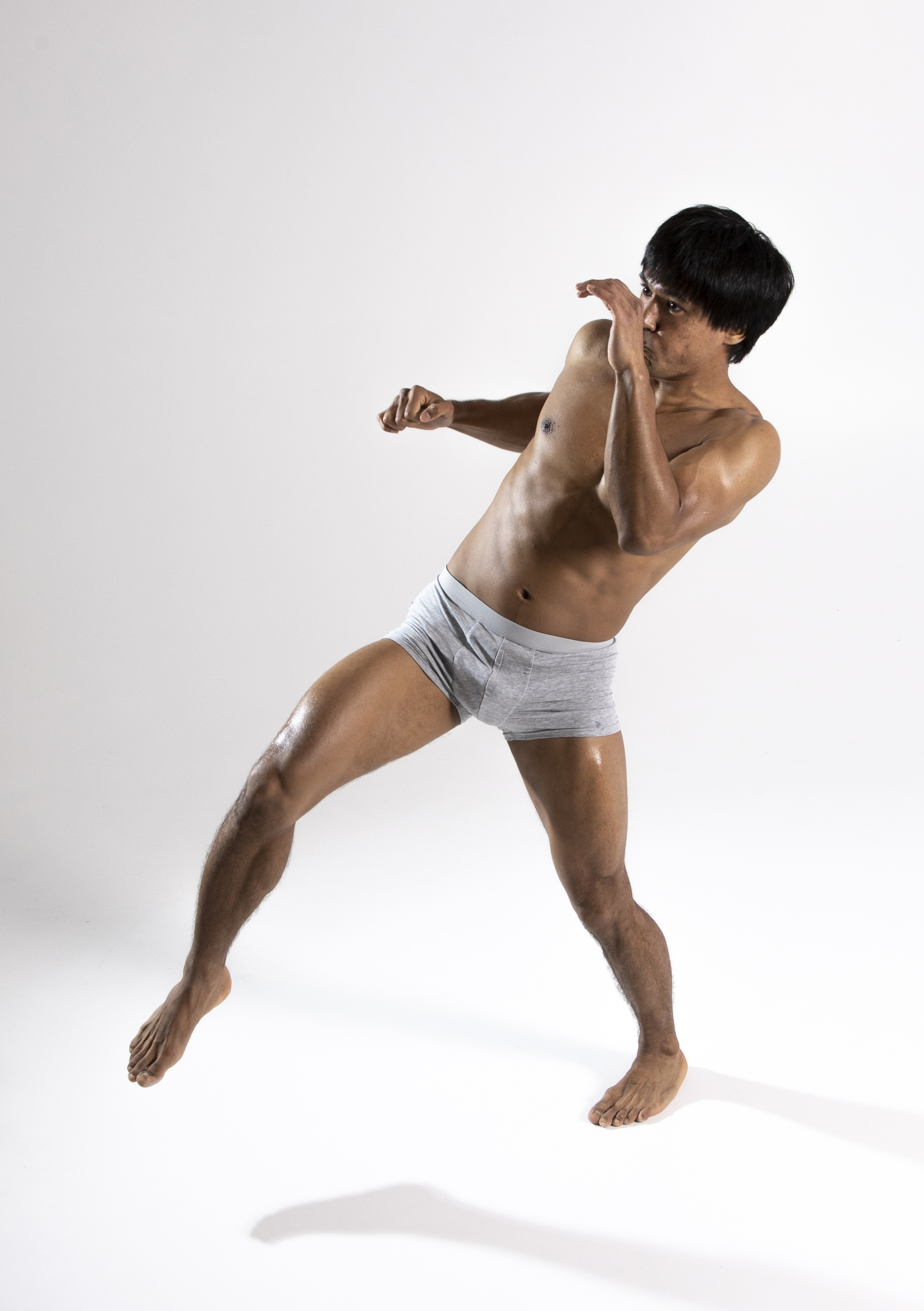 an athletic, asian man is wearing boxer briefs and is striking a fighting pose. he is barefoot and his skin is shiny.