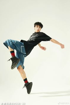 a young man in streetwear strikes a dynamic breakdancing pose against a white studio backdrop. he wears a black tshirt, denim shorts, and sneakers, showcasing athleticism and energetic movement. the image captures the essence of hiphop dance and youthful energy.