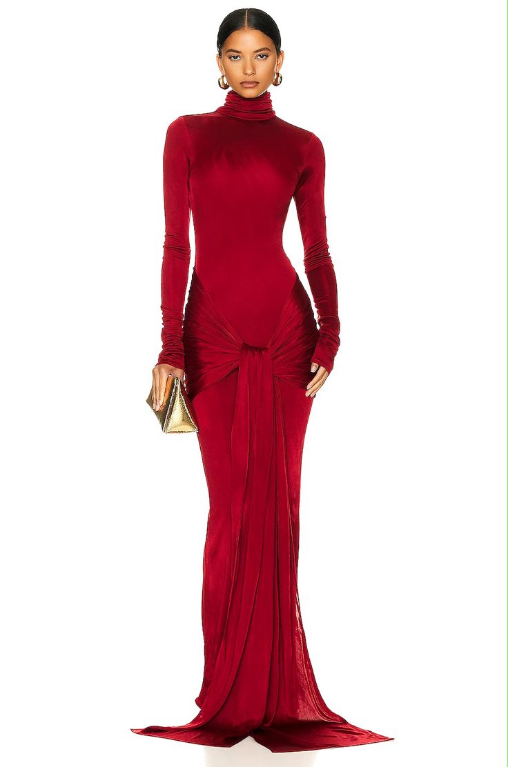 a full shot of a woman in a long, red, silk jersey gown. the dress has a turtleneck, long sleeves, and a draped design around the waist. the model is posing against a white background.