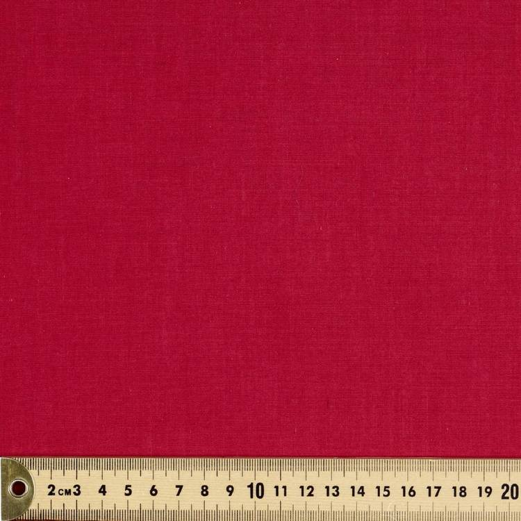 the image shows a flat lay of vibrant red fabric. a wooden ruler with centimeter markings is placed at the bottom of the image, indicating the fabric's size and scale. the fabric has a smooth, matte finish and appears to be suitable for sewing or crafts.