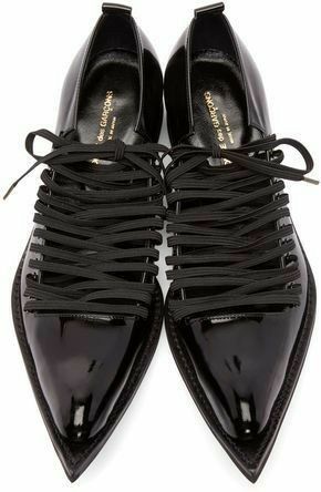 a topdown view of a pair of black, shiny leather shoes with pointed toes. the shoes feature a multistrap design with thin black straps crisscrossing the upper part of the shoe. the laces are tied loosely at the top. the shoes are identified as comme des garcons.