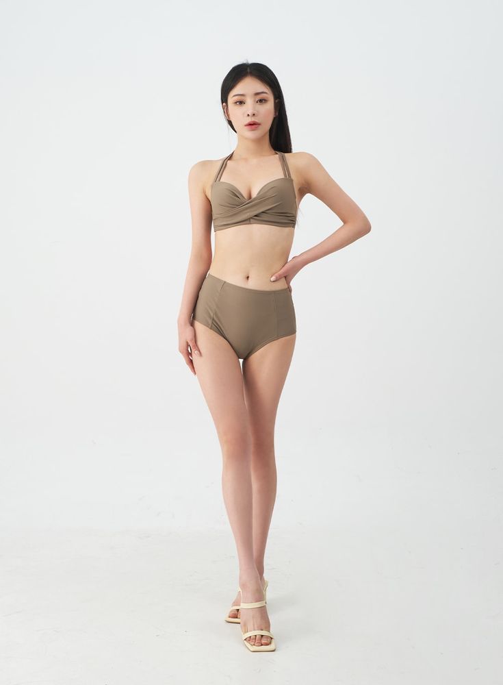a fullbody shot of a young, slender asian woman posing in a taupecolored twopiece swimsuit. the swimsuit features a highwaisted bottom and a halter top with a twisted detail. the model is standing with a slight hand on hip pose, showcasing the swimsuit against a white background. she is wearing lightcolored, strappy highheeled sandals.  the overall image is clean and welllit, suggestive of a fashion catalog or online store product photography.