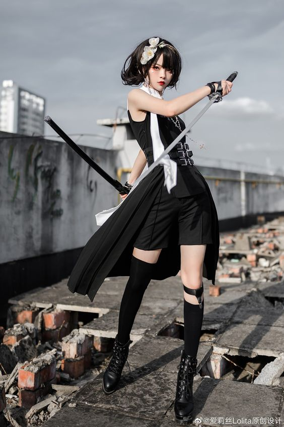 a young woman dressed in black clothing stands on a rooftop with rubble in the background. she holds a katana sword, its blade reflecting the sunlight. she wears black platform boots and has a black and white outfit accented with belts and straps. her hair is styled with a combination of black and brown, and she wears a determined expression on her face. the image is a cosplay portrait taken outdoors with natural lighting.