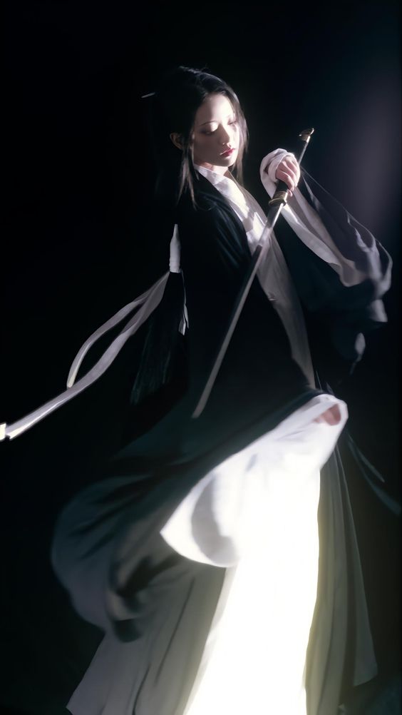 a woman in flowing white and black hanfu strikes a dynamic pose in a dark room illuminated by a spotlight. she holds a sword aloft in her right hand, the blade catching the light. her long, dark hair flows behind her as she spins, the movement creating a sense of action and power.