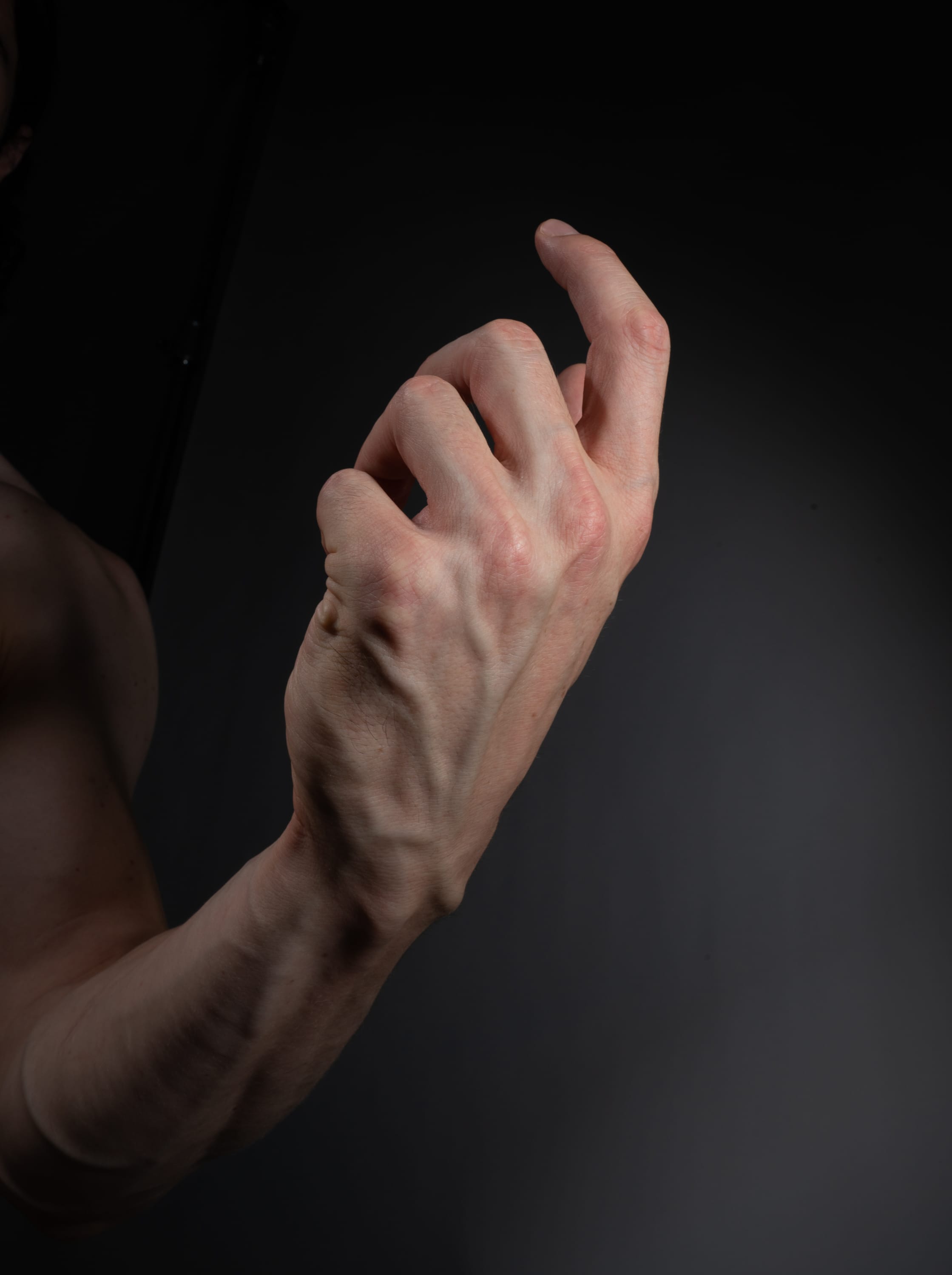 a closeup side view of a man's arm and hand, tensed and reaching forward against a dark gray background. the prominent veins and muscles highlight the physical exertion.