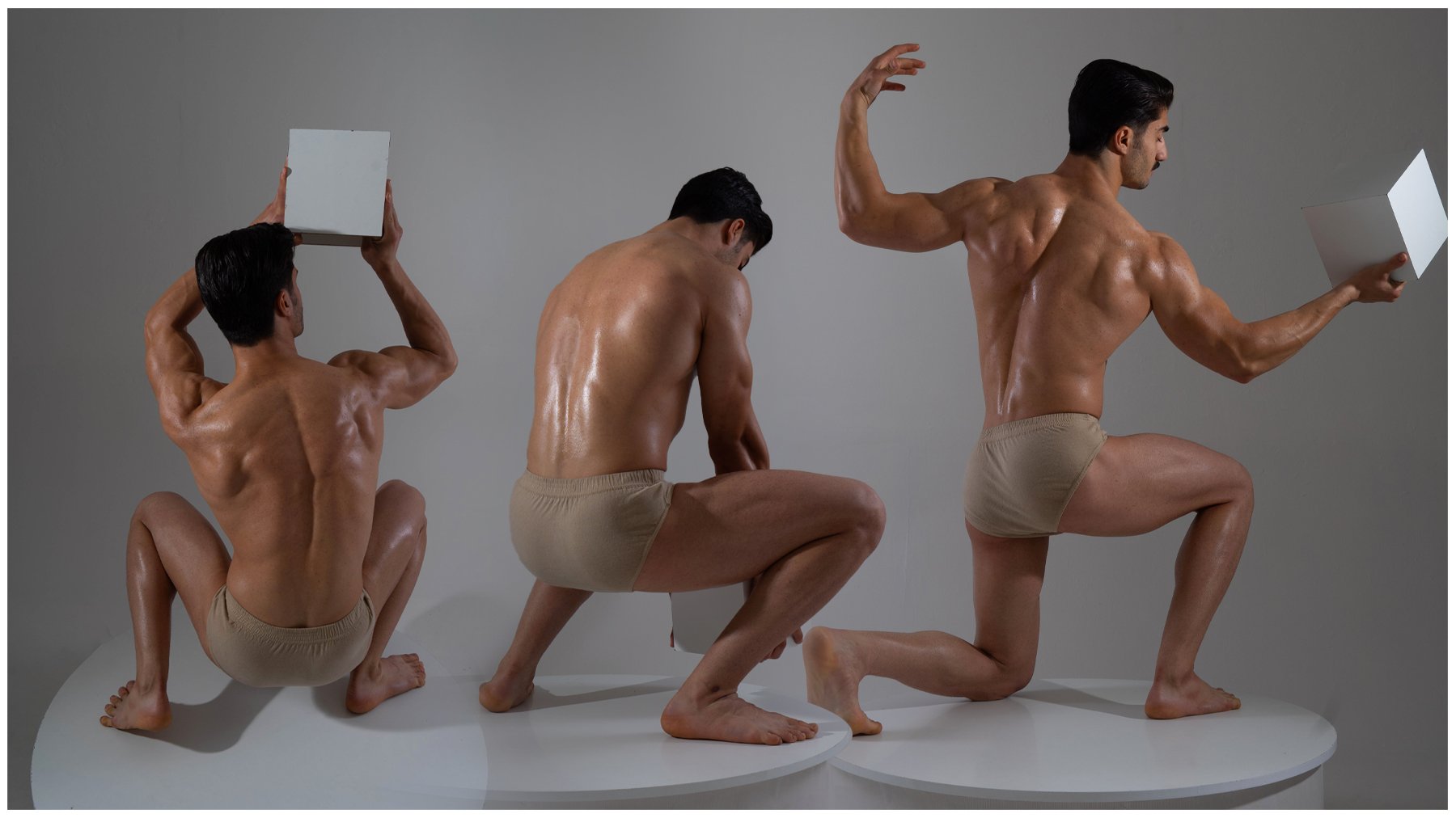 the image shows a muscular man in three different poses, seemingly part of an anatomical or figure study. he's nude except for a small garment, and his body appears oiled or wet, accentuating his physique. in each pose, he's positioned on a white circular platform against a light gray background. he's holding a white cube or rectangular prism in two of the poses. the image looks like it could be a sculpture or a photograph of a live model.