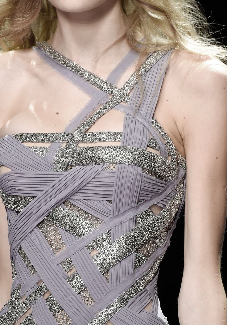 close up of a woman in a silver and grey strappy dress with beaded embellishments on the straps, showcasing the intricate detailing of the outfit. the model's hair is pulled back, revealing the neckline and emphasizing the luxurious fabric and delicate design. the overall image is a testament to high fashion and sophisticated style.
