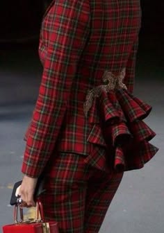 a woman wearing a red and green plaid suit with a ruffled hem. the jacket has a tailored fit and is cinched at the waist. the pants are also tailored and have a slim fit. the woman is standing in a casual pose, and her outfit is very stylish and trendy. this outfit would be perfect for a formal event or a night out on the town.