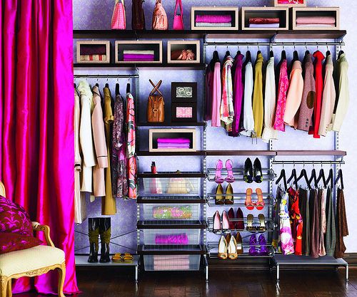 an organized closet featuring clothing on hangers, shelves with shoes, purses, and folded items, drawers, a chair with pillows, and a vibrant pink curtain.