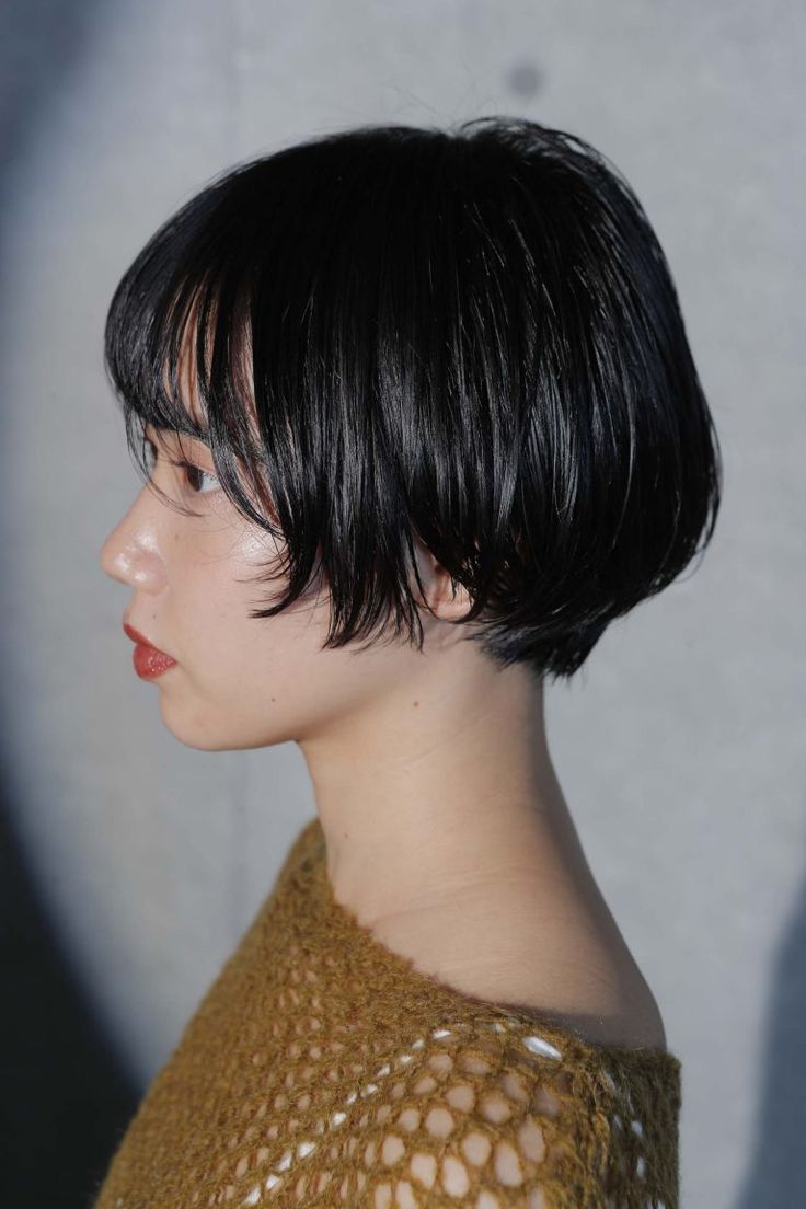 a young asian woman with short black hair is looking away from the camera. her hair is cut in a bob style and she is wearing a brown knitted sweater. her lips are painted in a red lipstick.