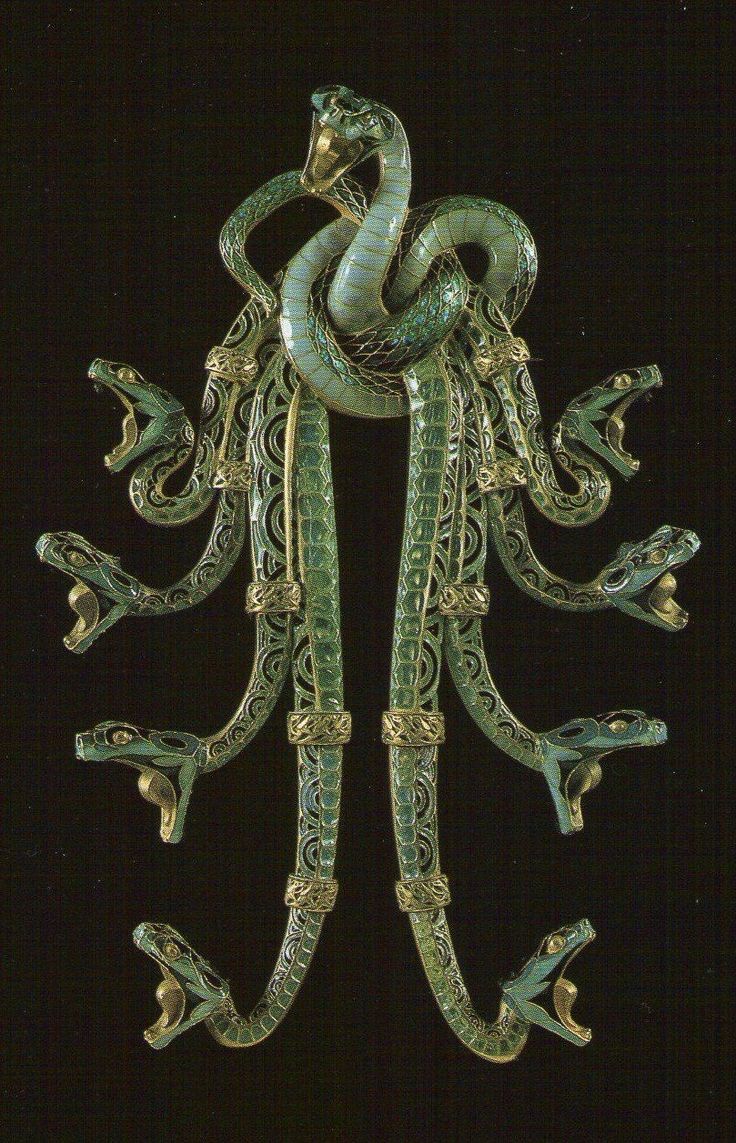 a close up image of a vintage snake brooch. the snake is made of gold and enamel and is very ornate. the snake is depicted with many heads, each with an open mouth, giving it a menacing appearance.