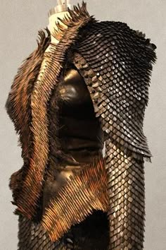 a closeup image of a detailed costume piece with scales. the scales are made of metal and leather, creating a futuristic and fantasy look. the costume is a mix of gold, brown and black colors and appears to be a piece of armor. the intricate detail of the scales makes the costume look like a work of art. the texture of the metal and leather is evident in the photo.