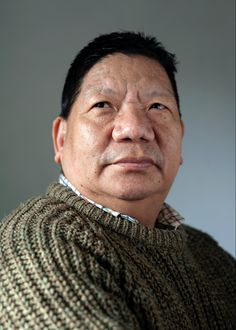 the image is a portrait of a middleaged man with short, dark hair and a serious expression. he is wearing a green, knit sweater. the background is a neutral gray. the lighting is soft and diffused, creating a sense of intimacy. the image is taken from an eyelevel perspective, making the viewer feel like they are on the same level as the subject.