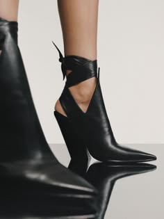 a woman's legs, from the knees down, are shown wearing black leather boots with a high stiletto heel. the boots are anklelength and feature a pointed toe and an ankle strap. the boots are cut out around the ankles to show the skin. the woman is wearing the boots with a casual outfit, and they look like they are comfortable and stylish. the boots are a classic style that can be dressed up or down.