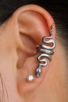 a closeup of an ear with a silver snake earring that wraps around the helix and conch, accompanied by a small, round stud in the earlobe.