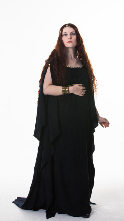 a fullbody shot of a woman with long red hair wearing a long, black, flowing dress that resembles ancient greek attire. she is adorned with a gold headband and several gold bracelets. the woman is posing against a white background, with a serious expression on her face.  the dress drapes elegantly and the overall image suggests a historical or fantasy theme.