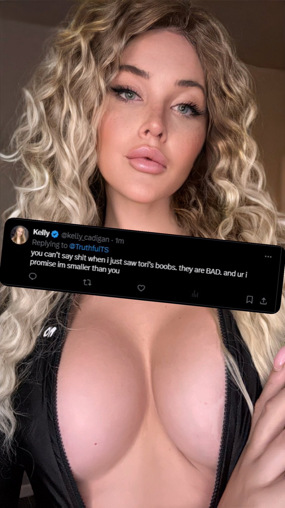 the image shows a blonde woman with large breasts in a lowcut black top taking a selfie.  a screenshot of a twitter post is superimposed on the image. the post is a reply to another user (@truthfults) and  comments on the size of someone else's breasts in comparison to her own, in a selfdeprecating and humorous way. the woman appears confident and comfortable in her own skin.  her hair is styled in loose curls. the overall tone of the image blends selfassuredness with a hint of playful banter about body image.