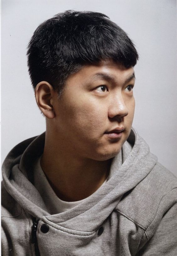 a studio portrait of an asian man with short black hair wearing a gray hoodie, he is looking off to the right side of the frame.