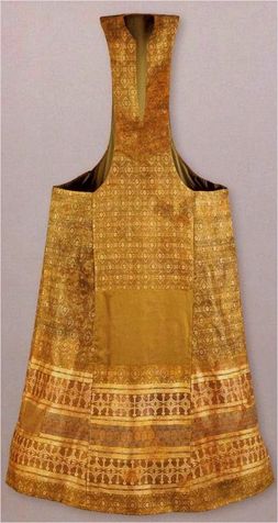 a golden chasuble is displayed. the chasuble is sleeveless and has a high neck with a slit. the textile of the chasuble is golden with ornate patterning.