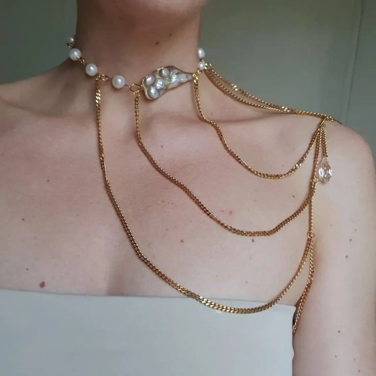 a person is wearing a pearl and gold chain necklace and shoulder jewelry set. the necklace features pearls and a baroque pearl element, with gold chains draping down over the shoulder. a clear crystal drop hangs from one of the chains.
