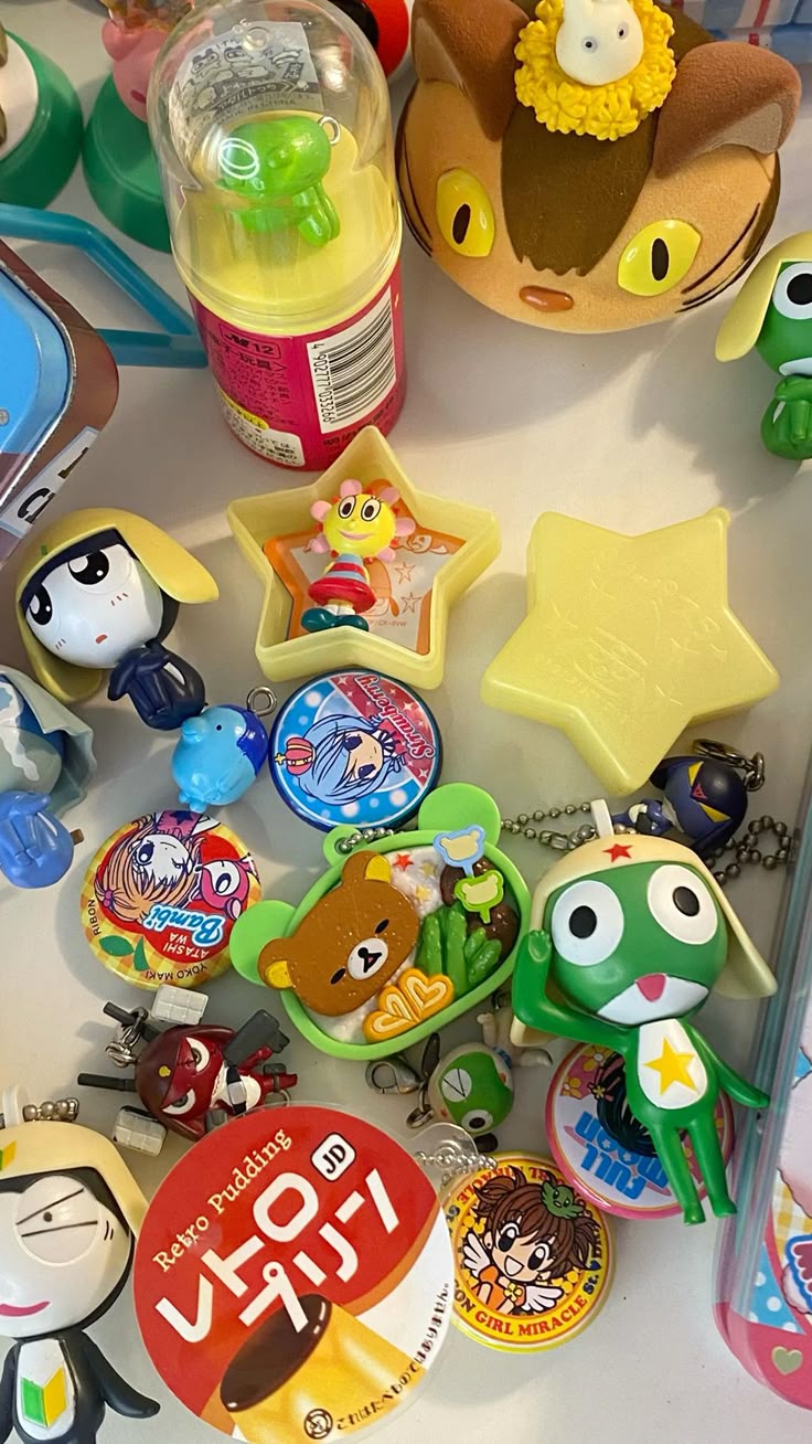 a collection of japanese toys and keychains featuring various cartoon and anime characters, alongside snack packaging, arranged on a white surface. there are figures of cats, frogs, and bears, along with starshaped items and keychains with different anime girl characters. several items are gashapon toys.