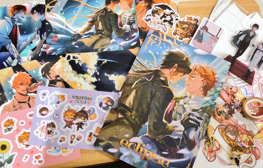 a close up shot of a table covered in various anime merchandise related to the characters tartaglia (childe) and zhongli from genshin impact. there are stickers featuring the characters, illustrations of them together, and a large print featuring them in an intimate pose labeled "eclipse".