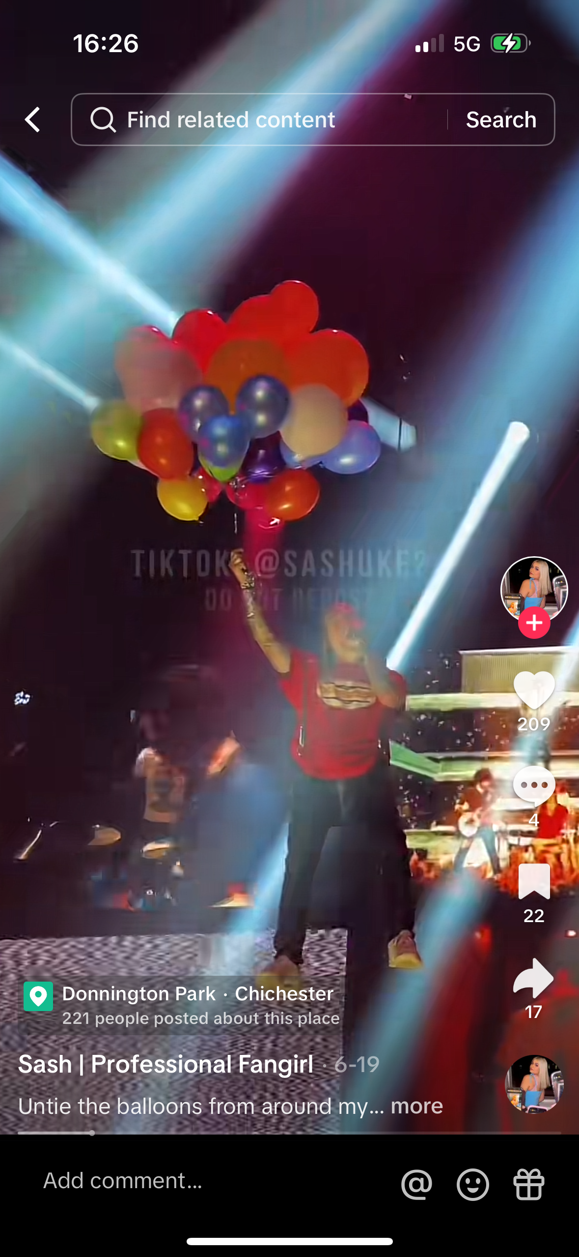 a woman in red shirt is holding a bunch of balloons, singing and dancing at a concert. she is surrounded by a crowd and brightly lit stage, as well as many spotlights. the image is from a tiktok video, which is playing in a mobile phone.