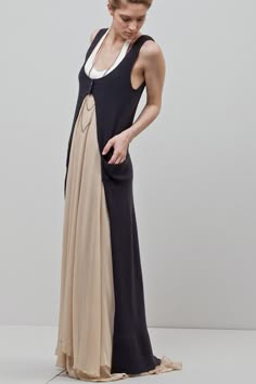 a beautiful woman with long black hair, wearing a long black sleeveless cardigan over a tan slip dress.  she is posing in a studio with a white background.