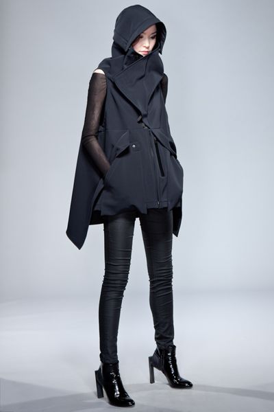 a woman model wearing a black hooded jacket with a black  pair of jeans and black boots. she is posing for a fashion shoot.