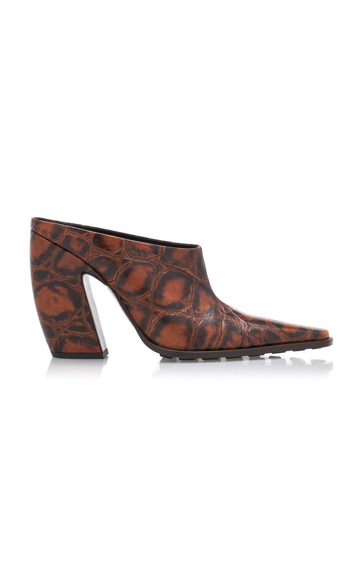 a pair of brown crocodile leather mules with a pointed toe and high block heel. the shoes are shown on a white background.