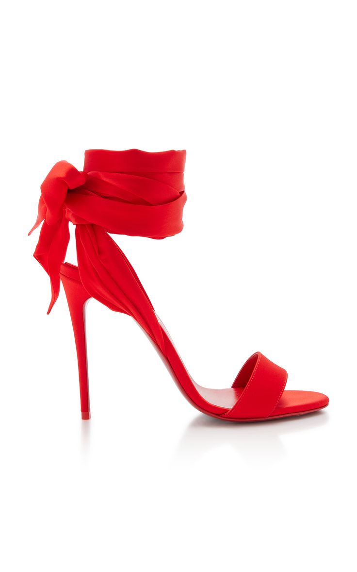 a pair of red satin high heel sandals with a ribbon ankle strap and bow detail. the shoes are on a white background.