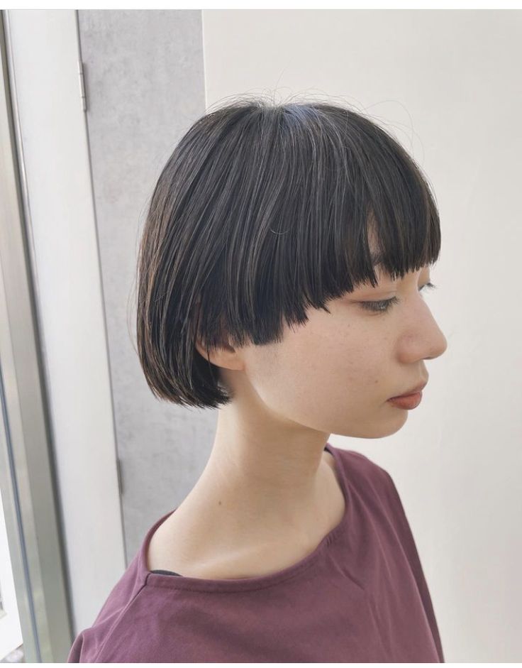 a young woman with black, straight hair, a blunt bob cut with blunt bangs is looking away from the camera.