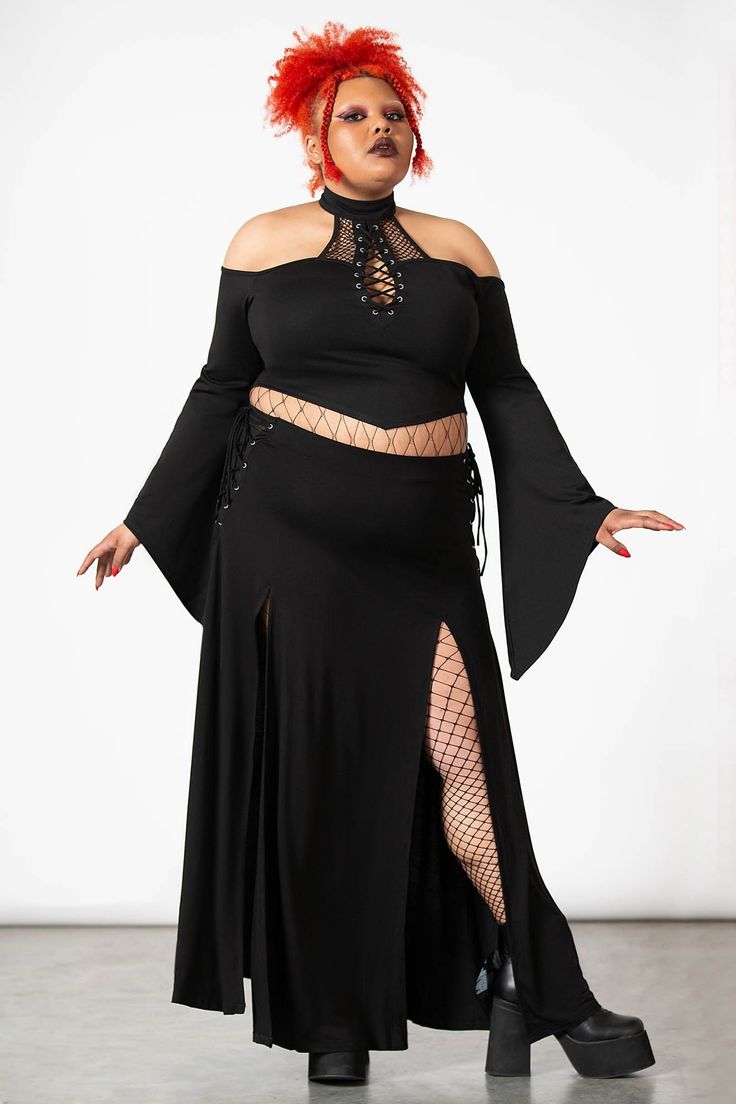 a plussize model with vibrant red hair is showcasing a black gothicinspired outfit. the ensemble consists of a black offtheshoulder top with laceup detailing at the neckline, paired with a highwaisted black maxi skirt featuring side slits. the skirt and top create a coordinated look, enhanced by the model's fishnet stockings and chunky black boots. the overall style is dark, elegant, and edgy, reflecting current gothic and alternative fashion trends. the image is professionally shot against a plain white background, highlighting the outfit's details and the model's pose.