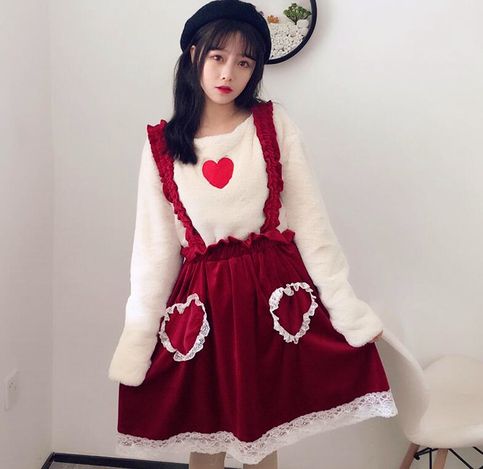 a young woman poses in a cute lolitastyle red dress with a white sweater underneath. the dress has white lace trim and heartshaped pockets. she is also wearing a black beret. the background is a plain white wall.