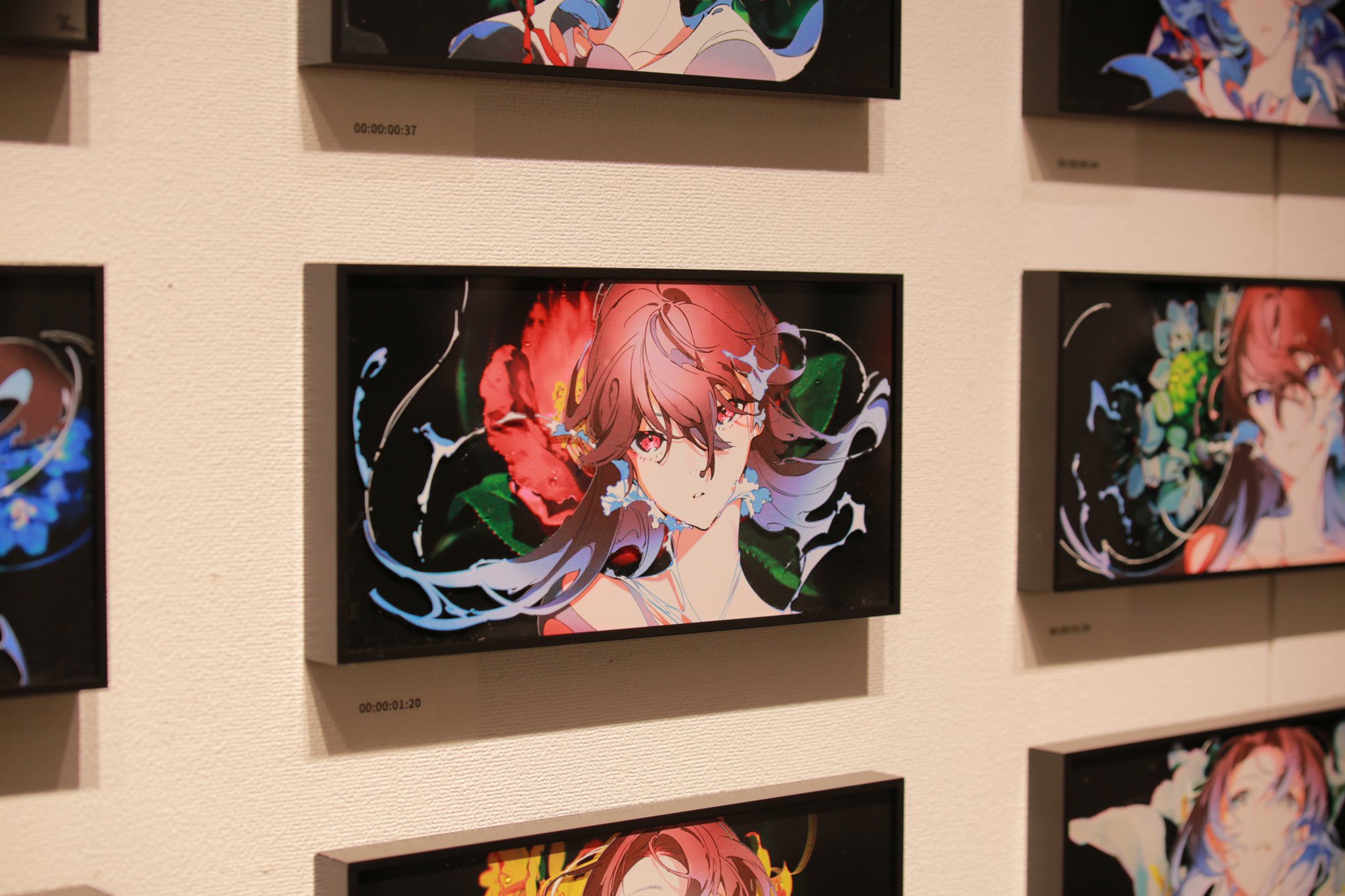 the image shows a collection of framed digital artwork displayed on a white wall in an art gallery. the artwork features a pinkhaired anime girl as the central subject.  the girl, depicted in a closeup portrait, has flowing pink hair and piercing red eyes. she is surrounded by vibrant floral patterns and abstract designs, with prominent use of blue and green hues. the artwork is brightly lit by artificial gallery lighting, creating a sense of vibrancy and highlighting the details of the digital illustrations.