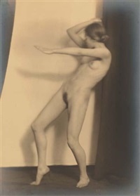 the image is a vintage black and white photograph of a nude female figure. the woman is positioned in a dynamic pose, appearing to be midmovement or dance. her body is elegantly curved, with her arms extended and head slightly tilted.  the background consists of a lightcolored wall and a darker vertical element, possibly a curtain or wall section, providing contrast. the photograph's style suggests a studio setting with careful lighting that creates dramatic shadows and highlights the contours of the woman's body.  the overall tone is artistic and evocative.